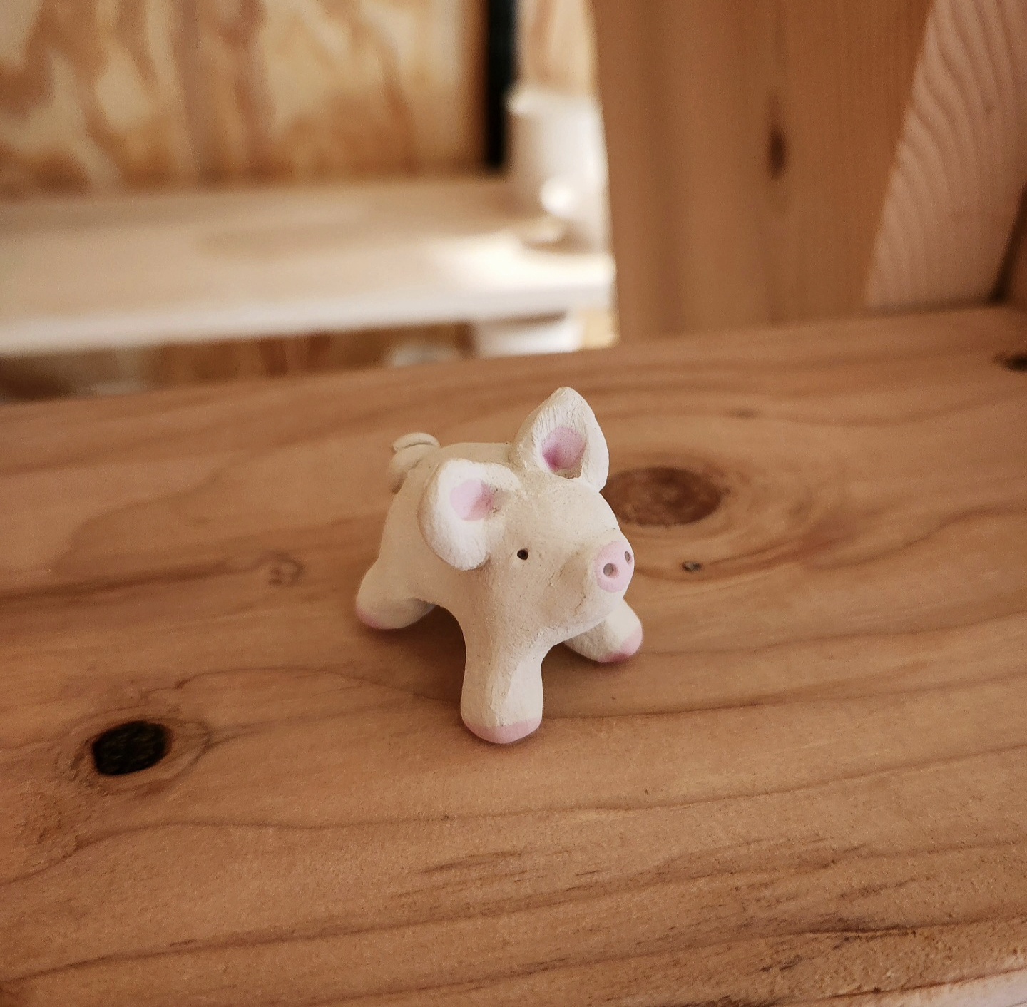 Tiny handbuilt clay pig figurine on a warm wood surface