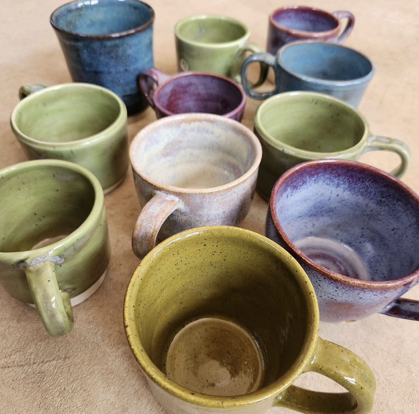 Overhead view of twelve handmade mugs in greens, blues, and purples