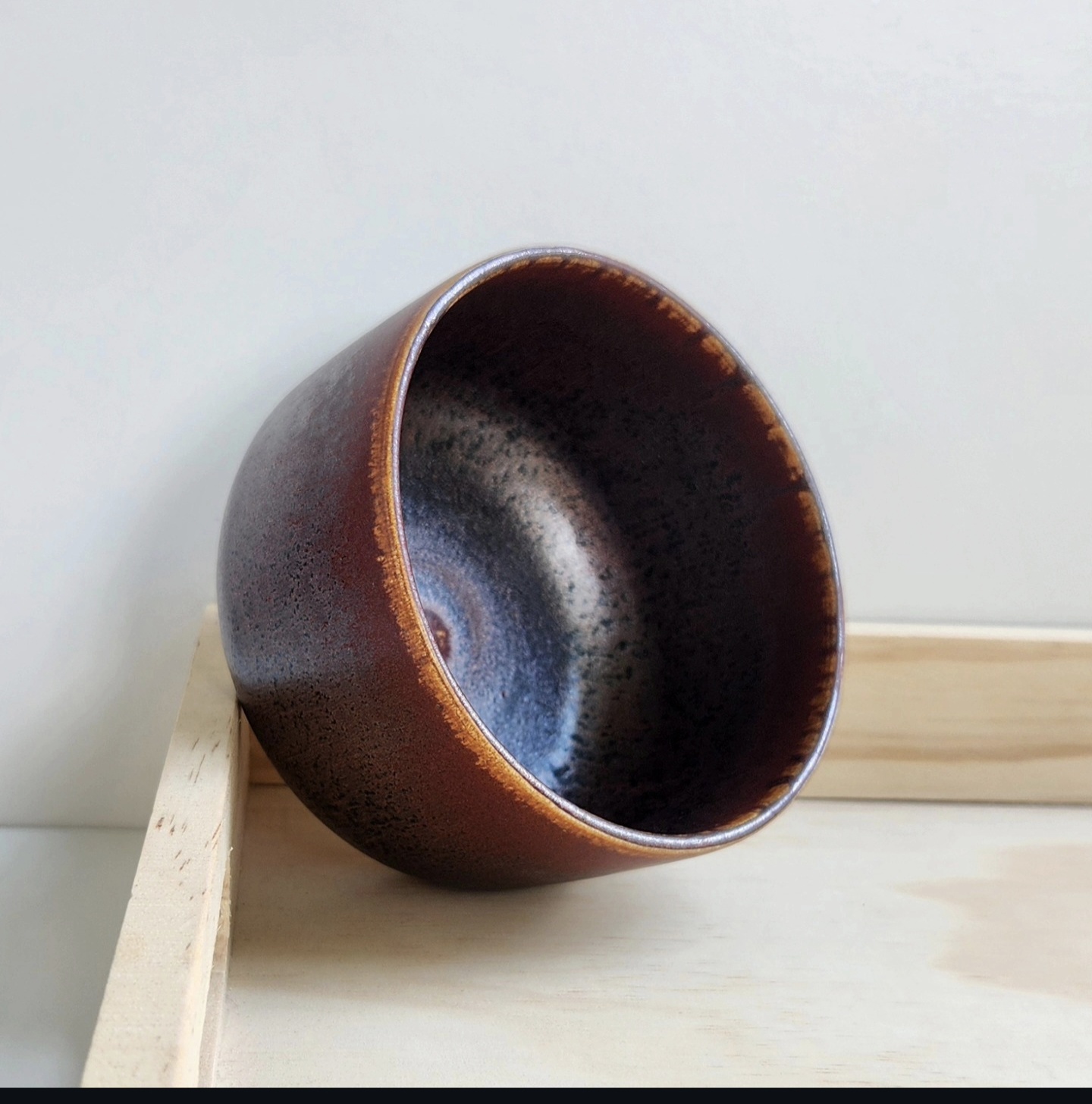Deep rust and midnight glazed bowl resting on a pine shelf