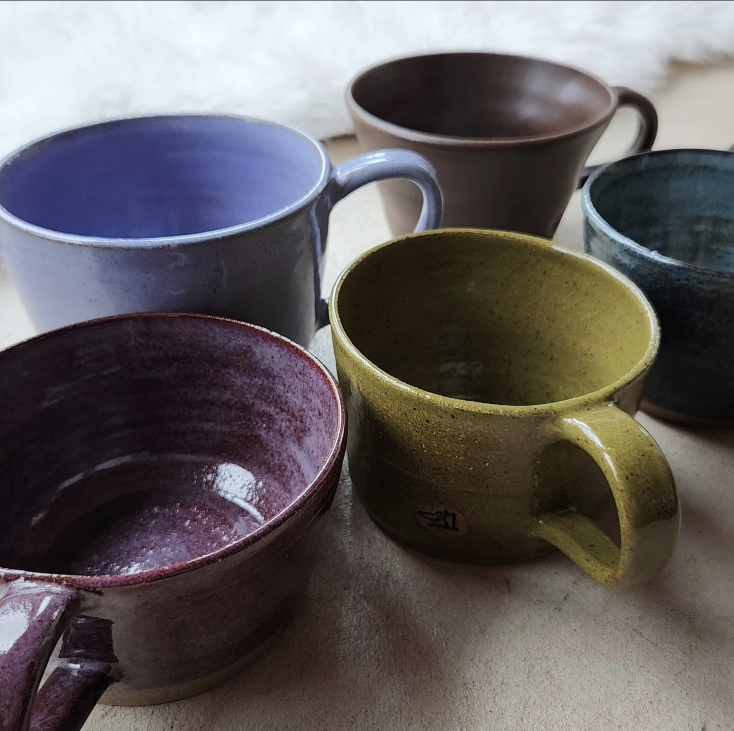 Five mugs in lavender, chocolate, olive, plum, and teal on a neutral surface